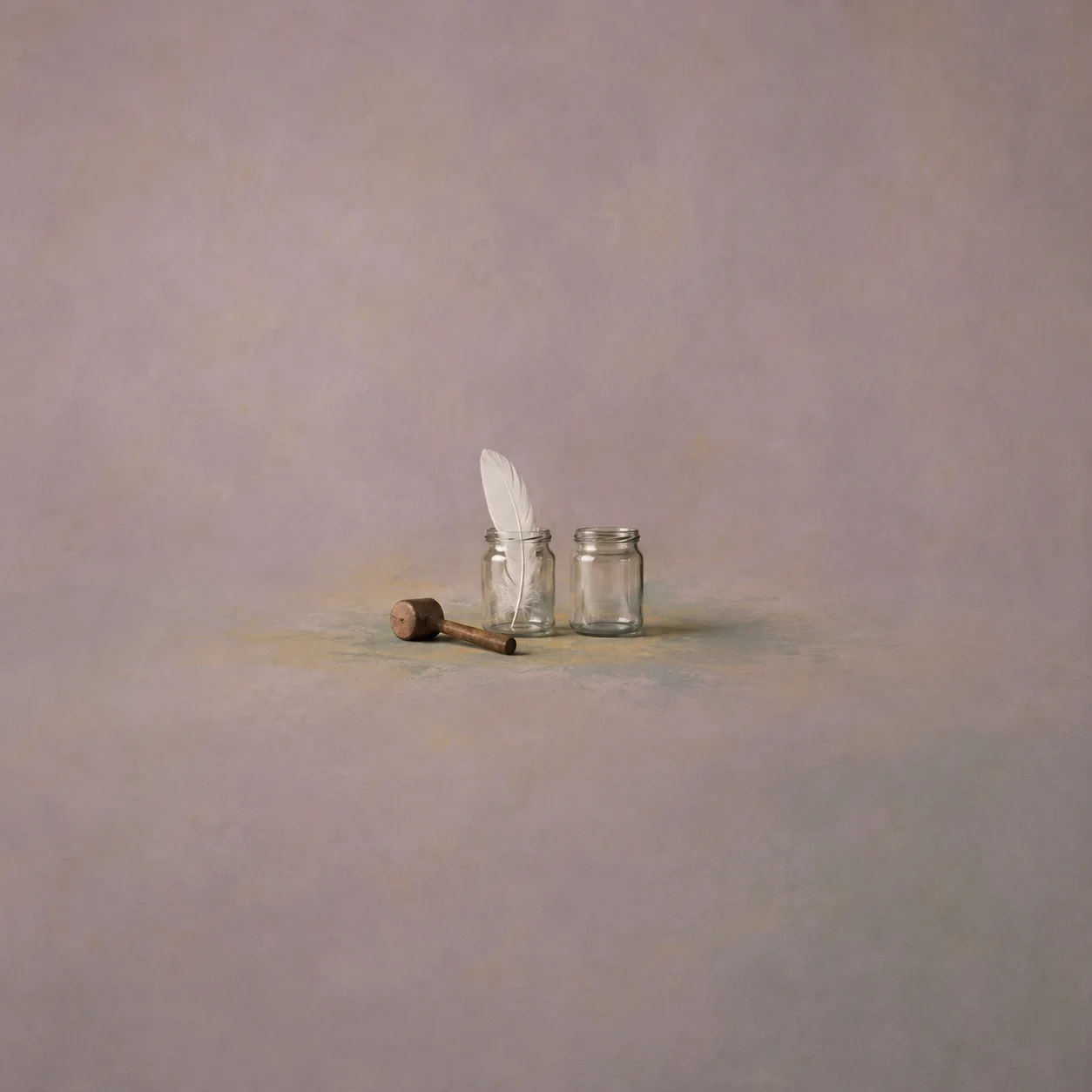 A wooden mallet beside two glass jars, one holding a white feather and the other empty.